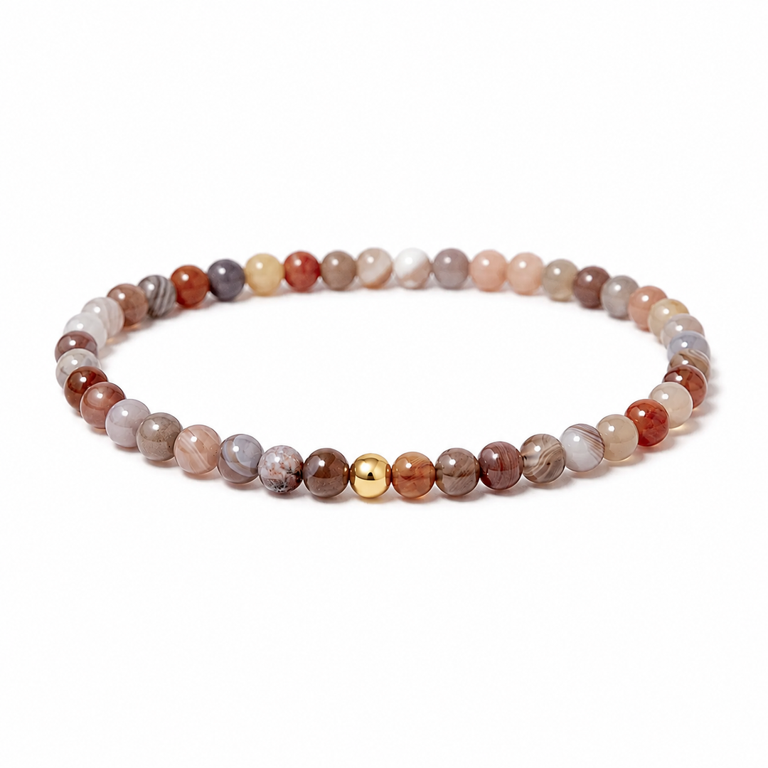 A beaded stretch bracelet made of polished round stone beads in earthy brown, beige, gray, and white tones, with a single small gold bead accent at the front, shown on a plain white background.