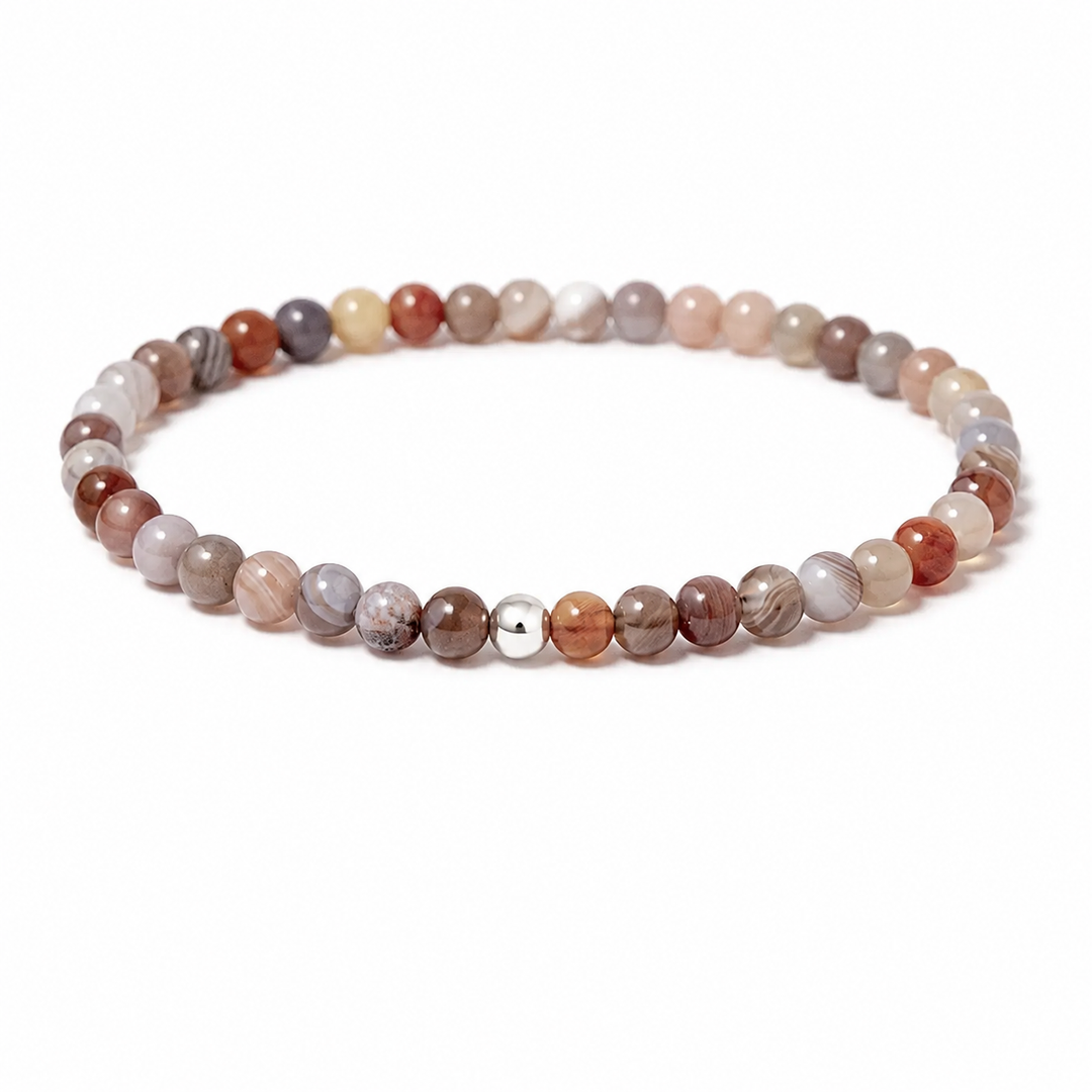 A beaded stretch bracelet made of polished round gemstone beads in earthy tones of brown, beige, gray, and white, with a single small metallic silver bead accent, shown on a plain white background.