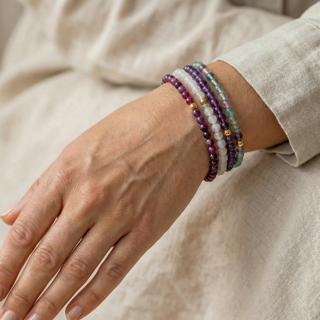 Close-up of a hand wearing multiple beaded bracelets on a neutral background