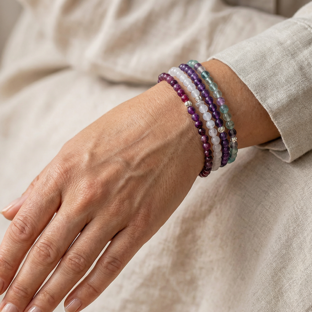 Close-up of a hand wearing multiple beaded bracelets on a neutral background
