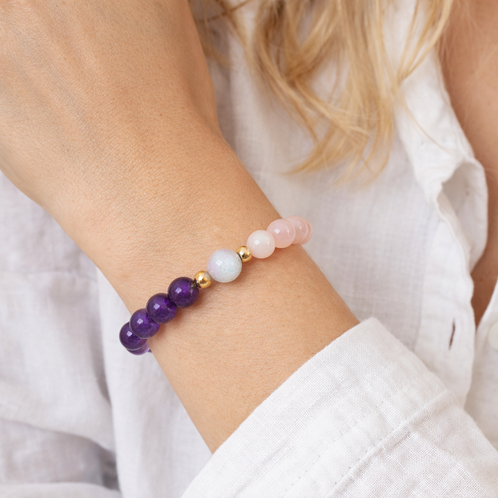 Beaded bracelet with purple, pink, and gold beads on a wrist against a white background