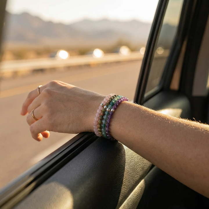 Person's hand with colorful bracelets on a car window, with a scenic road in the background