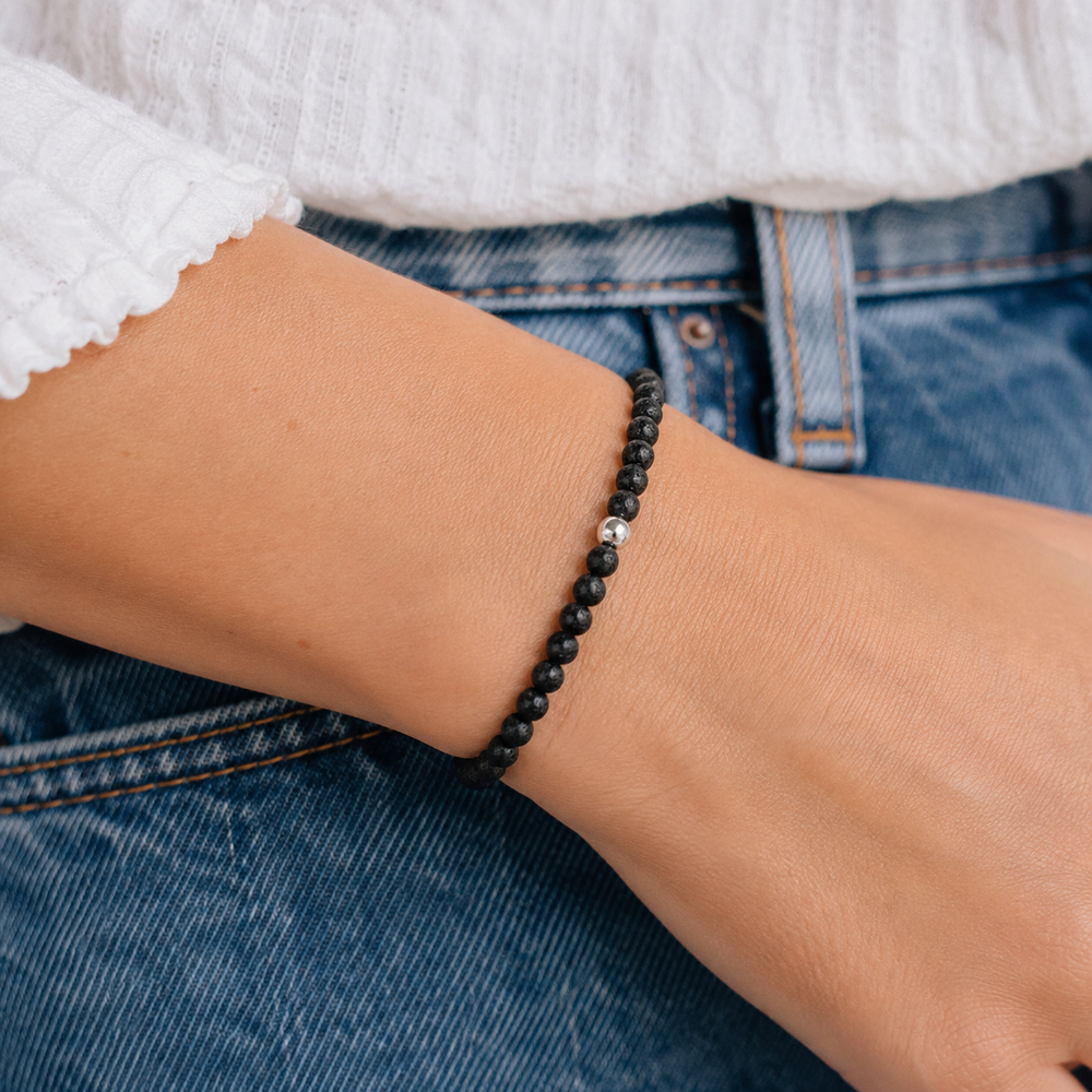 A close-up of a person's wrist wearing a beaded bracelet with black round beads and a small silver accent bead, styled with a white top and blue jeans.