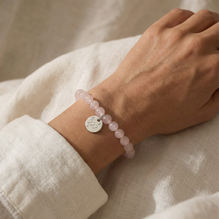 Hand wearing a pink beaded bracelet with a silver charm on a neutral background