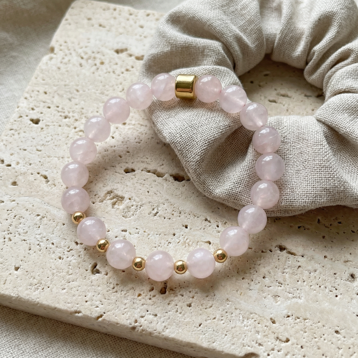 Pink beaded bracelet with gold accents on a textured surface